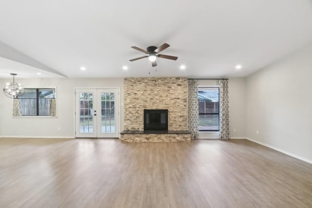 unfurnished living room with ceiling fan with notable chandelier, wood-type flooring, a large fireplace, and french doors