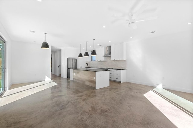 kitchen with dark countertops, wall chimney exhaust hood, open floor plan, and a sink