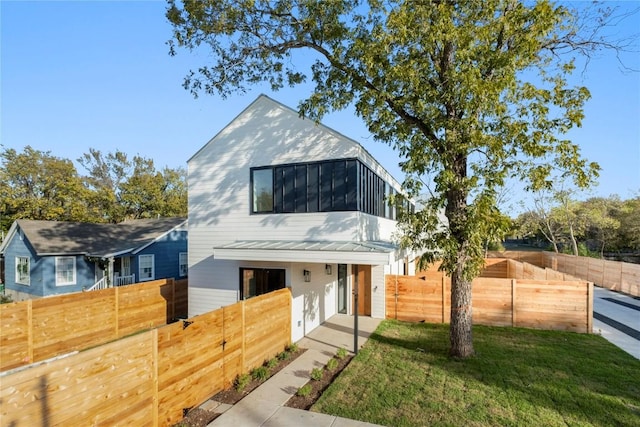 modern home featuring a front lawn, fence private yard, a sunroom, and metal roof