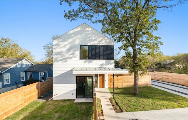 exterior space with a standing seam roof, fence private yard, a yard, and metal roof