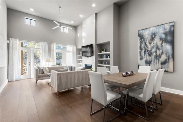 dining room featuring built in features, a large fireplace, dark hardwood / wood-style flooring, a high ceiling, and french doors