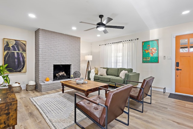 living room with ceiling fan, a brick fireplace, and light wood-type flooring