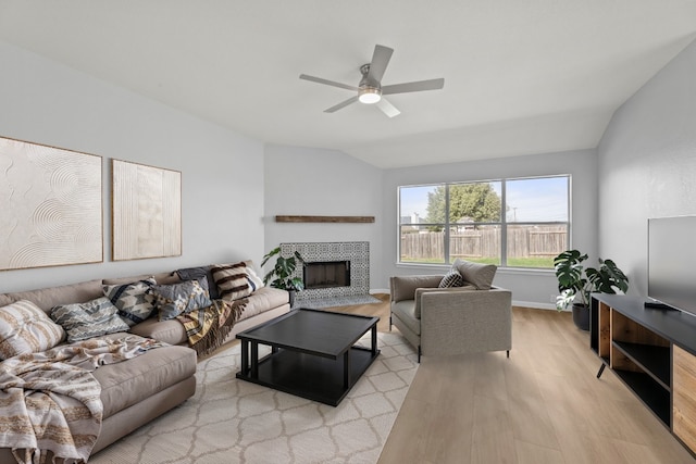 living room featuring light wood-type flooring, vaulted ceiling, a tile fireplace, and ceiling fan