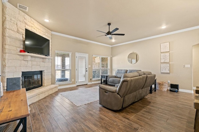 living room with hardwood / wood-style flooring, ceiling fan, a stone fireplace, and crown molding