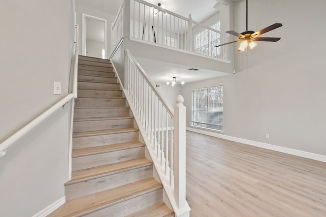 staircase with a towering ceiling, hardwood / wood-style floors, and ceiling fan