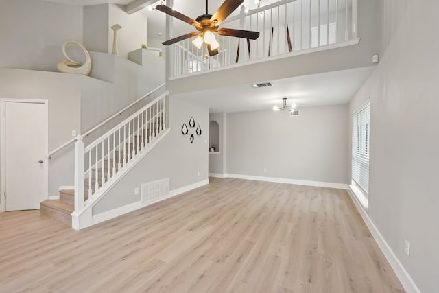 unfurnished living room featuring light hardwood / wood-style flooring, ceiling fan, and a high ceiling