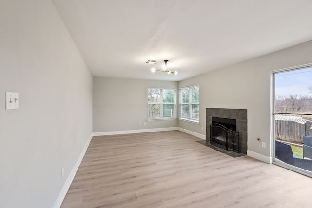 unfurnished living room with a notable chandelier, a tile fireplace, and light wood-type flooring