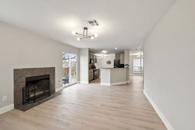 unfurnished living room with a tiled fireplace, light hardwood / wood-style floors, and a notable chandelier