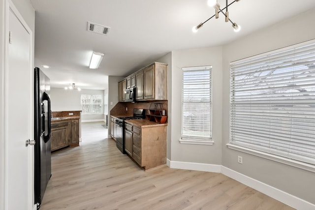 kitchen with tasteful backsplash, dark stone countertops, black appliances, an inviting chandelier, and light hardwood / wood-style flooring