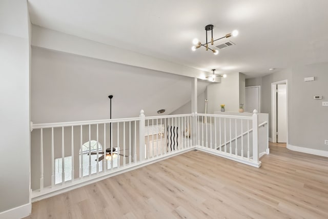 spare room with ceiling fan with notable chandelier and light hardwood / wood-style flooring