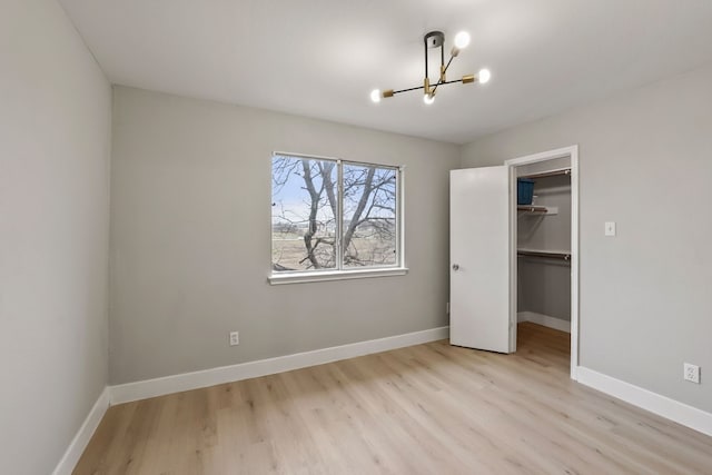 unfurnished bedroom with a closet, a spacious closet, light hardwood / wood-style flooring, and a notable chandelier