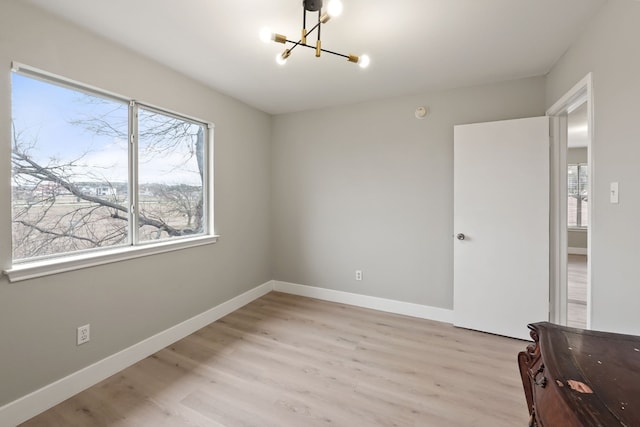 spare room featuring a notable chandelier, light wood-type flooring, and a wealth of natural light