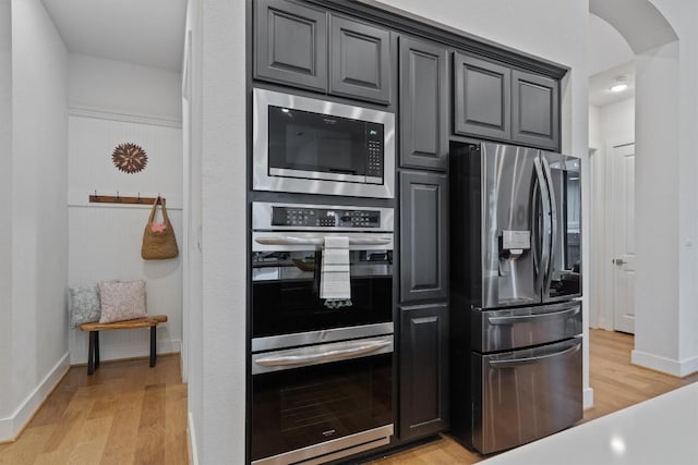 113 University Lands Dr, Liberty Hill, TX 78642 - kitchen with appliances with stainless steel finishes, baseboards, light wood-style floors, arched walkways, and gray cabinetry