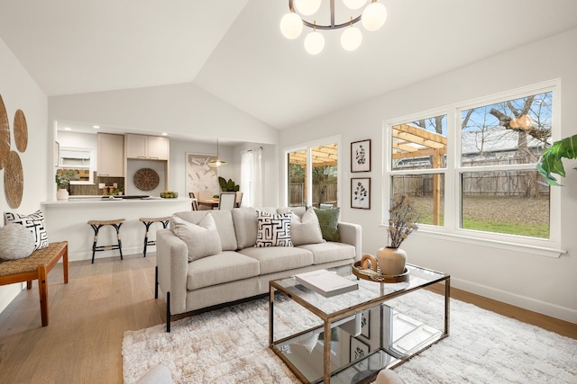 living room with an inviting chandelier, light hardwood / wood-style flooring, and vaulted ceiling