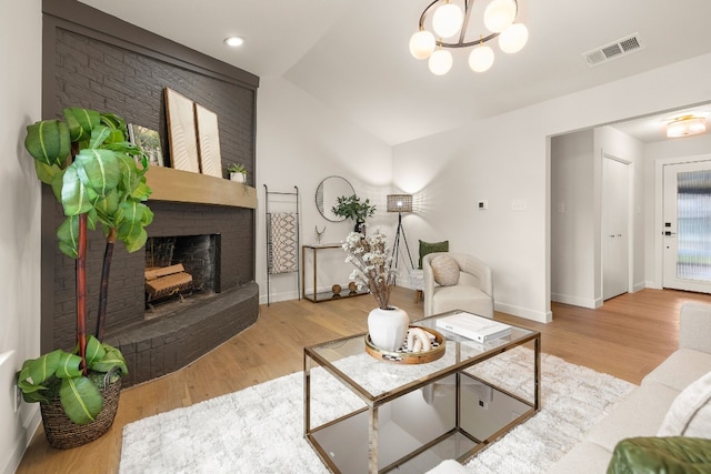 living room featuring an inviting chandelier, lofted ceiling, a fireplace, and light wood-type flooring