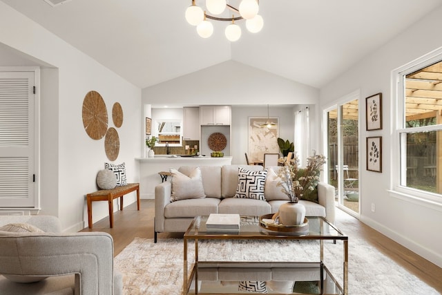 living room featuring lofted ceiling, plenty of natural light, a chandelier, and light hardwood / wood-style flooring