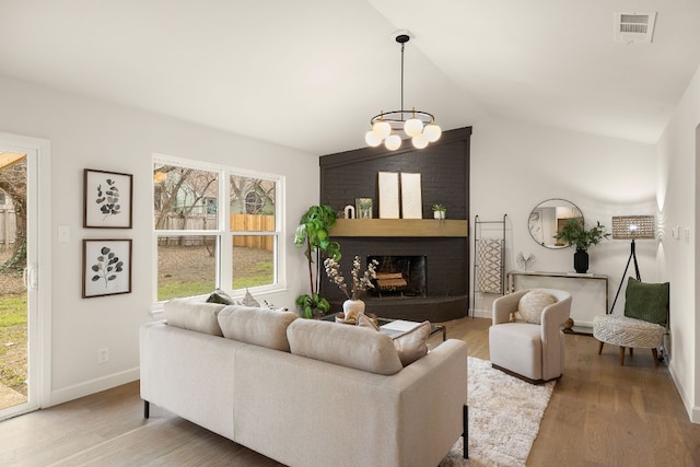 living room with lofted ceiling, hardwood / wood-style flooring, a fireplace, and an inviting chandelier