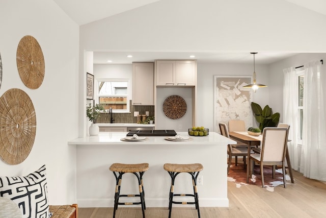 kitchen with decorative light fixtures, lofted ceiling, backsplash, kitchen peninsula, and light wood-type flooring