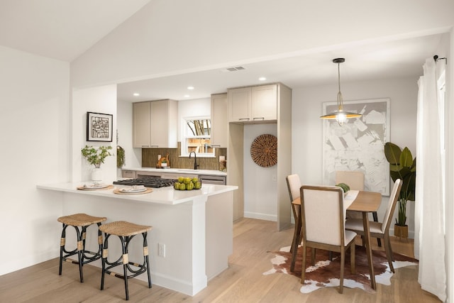 kitchen featuring lofted ceiling, hanging light fixtures, tasteful backsplash, kitchen peninsula, and light wood-type flooring