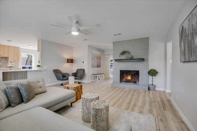 living room with ceiling fan, a brick fireplace, and light hardwood / wood-style flooring