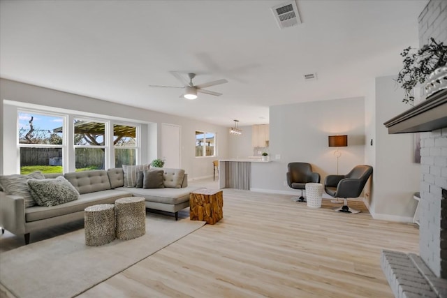 living room with ceiling fan, a brick fireplace, and light hardwood / wood-style floors