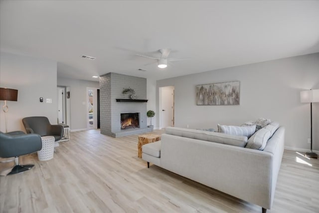 living room with ceiling fan, a brick fireplace, and light hardwood / wood-style floors