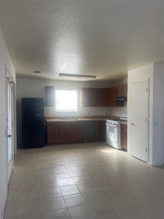 kitchen featuring white gas range, sink, black fridge, and a textured ceiling