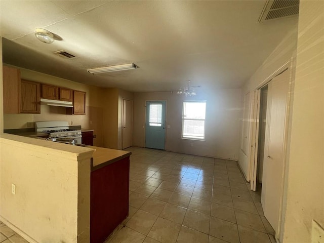 kitchen with light tile patterned floors, white gas range oven, and kitchen peninsula