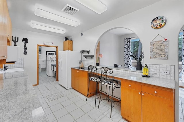 kitchen with sink, light stone counters, white refrigerator with ice dispenser, light tile patterned flooring, and washer / clothes dryer