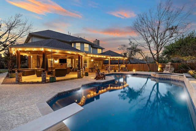 pool at dusk featuring a diving board, a patio area, exterior kitchen, and exterior bar