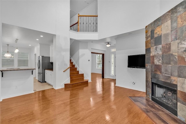 living room featuring a towering ceiling, a tile fireplace, and light wood-type flooring