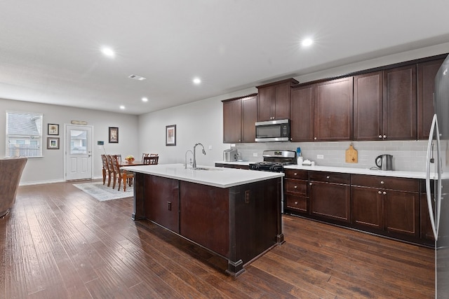 7716 Arezzo Dr, Round Rock, TX 78665 - kitchen featuring appliances with stainless steel finishes, light countertops, a kitchen island with sink, dark wood-type flooring, and tasteful backsplash
