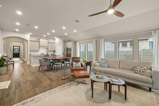 living room with ceiling fan, vaulted ceiling, and light wood-type flooring