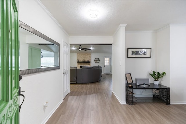 hallway with ornamental molding, a textured ceiling, and light wood-type flooring