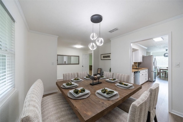 dining space featuring ornamental molding, sink, and light hardwood / wood-style flooring