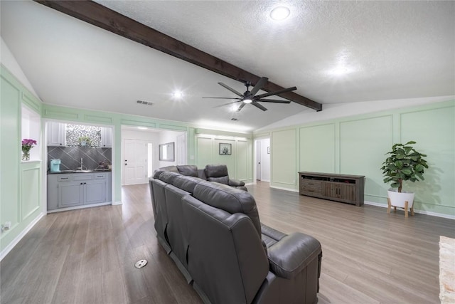 living room featuring ceiling fan, a textured ceiling, light hardwood / wood-style flooring, and vaulted ceiling with beams