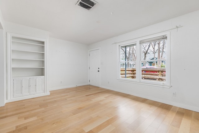 empty room featuring built in shelves and light wood-type flooring