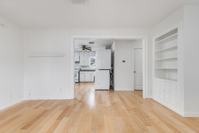 unfurnished living room featuring built in shelves, light hardwood / wood-style flooring, and ceiling fan