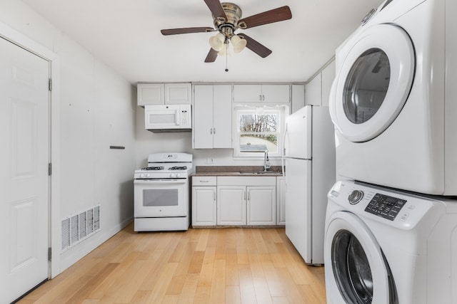 kitchen featuring sink, white cabinets, stacked washer and clothes dryer, light hardwood / wood-style floors, and white appliances