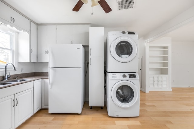 laundry room featuring stacked washer and dryer, sink, ceiling fan, and light hardwood / wood-style flooring