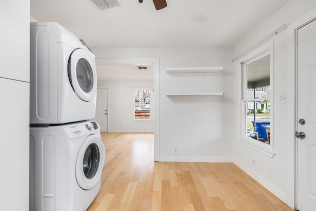 washroom featuring ceiling fan, stacked washer and clothes dryer, plenty of natural light, and light hardwood / wood-style floors