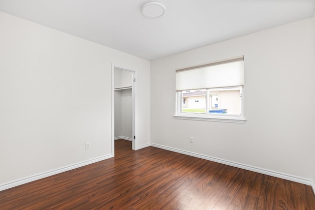 unfurnished bedroom featuring a spacious closet, dark wood-type flooring, and a closet