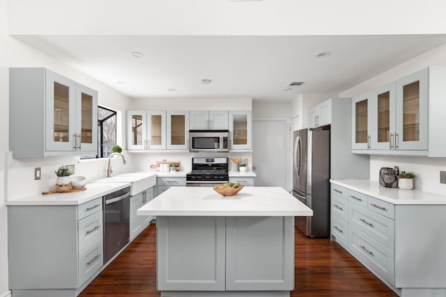 kitchen with sink, appliances with stainless steel finishes, dark hardwood / wood-style floors, gray cabinets, and a kitchen island