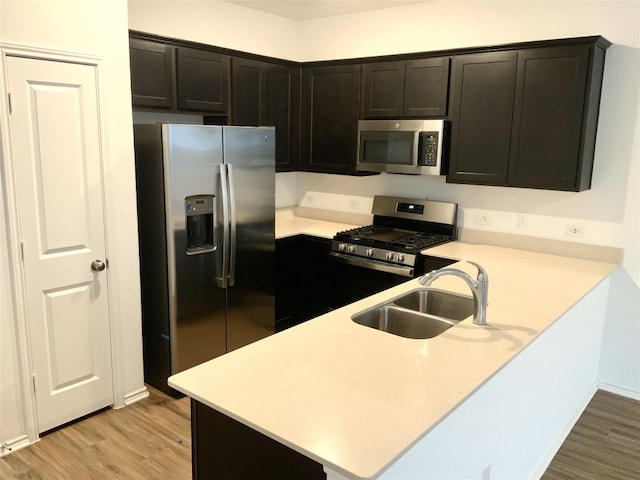 kitchen with sink, light wood-type flooring, kitchen peninsula, and appliances with stainless steel finishes