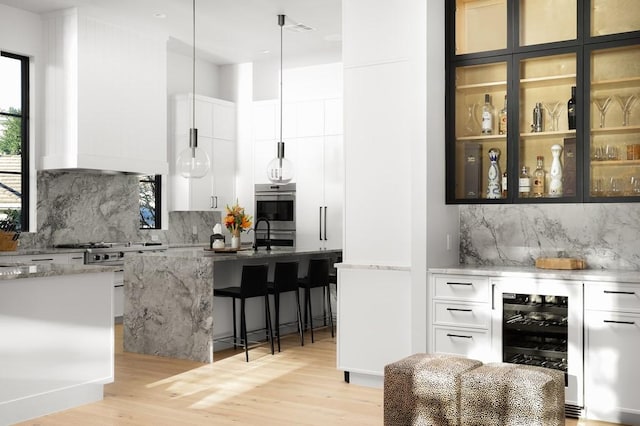 bar featuring white cabinetry, light stone counters, decorative light fixtures, light hardwood / wood-style flooring, and beverage cooler