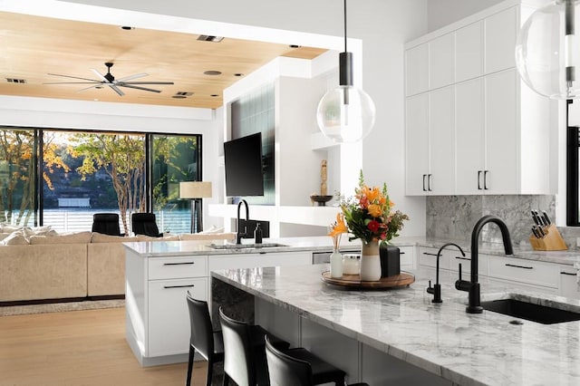 kitchen featuring pendant lighting, sink, light stone counters, and white cabinets