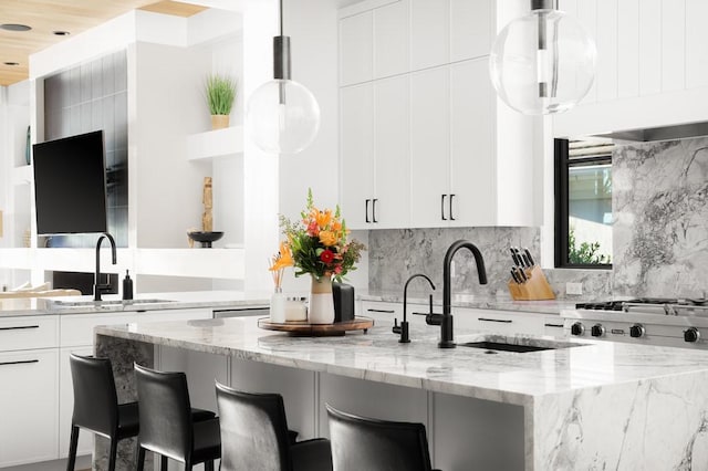 kitchen with a breakfast bar, white cabinetry, sink, hanging light fixtures, and light stone counters