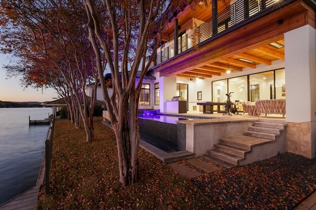 patio terrace at dusk featuring a hot tub, a balcony, and a water view