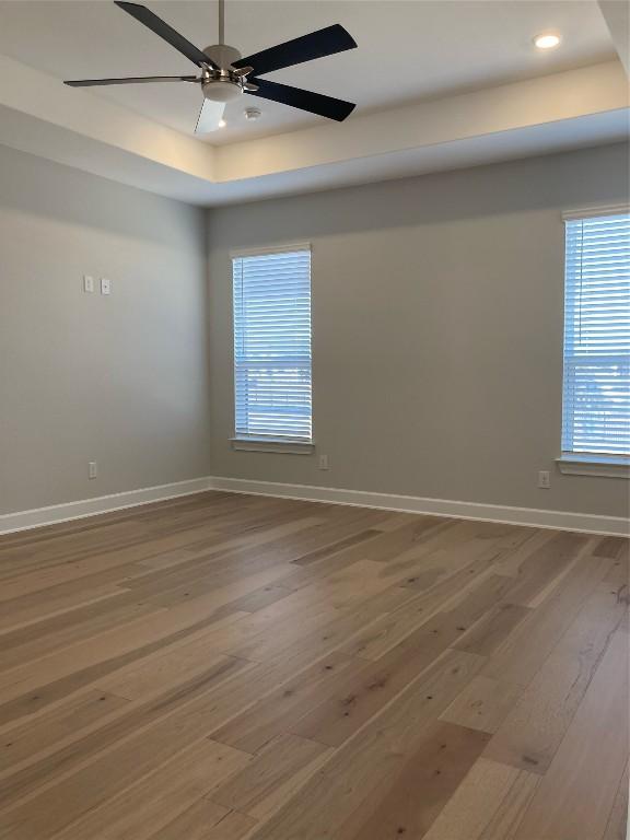 unfurnished room featuring hardwood / wood-style floors, a tray ceiling, and ceiling fan