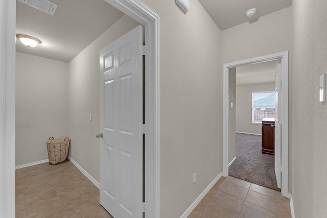 corridor featuring light tile patterned floors, visible vents, and baseboards